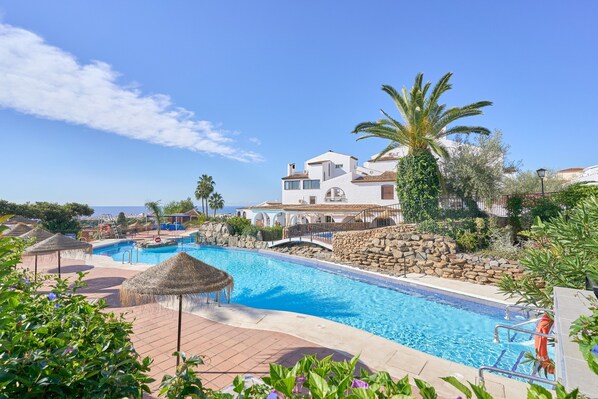 A swimming pool with a stone wall, palm trees, and a building in the background.