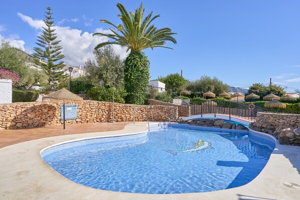 A swimming pool with a stone wall, palm trees, and a clear blue sky.