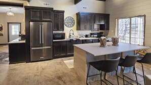 Una cocina moderna con armarios oscuros, electrodomésticos de acero inoxidable y una isla central con taburetes de bar.