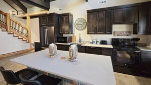 Una cocina moderna con armarios de madera oscura, una isla grande con dos jarrones decorativos, un reloj y una escalera que conduce a un área estilo loft.
