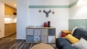 Un espacio habitable compacto con kitchenette, un sofá con cojines, una mesa de centro y un elemento decorativo en la pared.