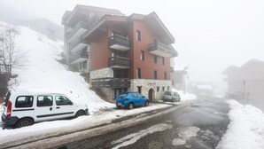 Un edificio con varios balcones, una calle cubierta de nieve y vehículos estacionados.