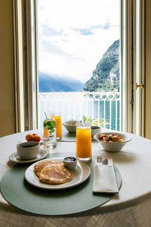A breakfast table with pancakes, a bowl of fruit, a pitcher of orange juice, and a glass of orange juice.
