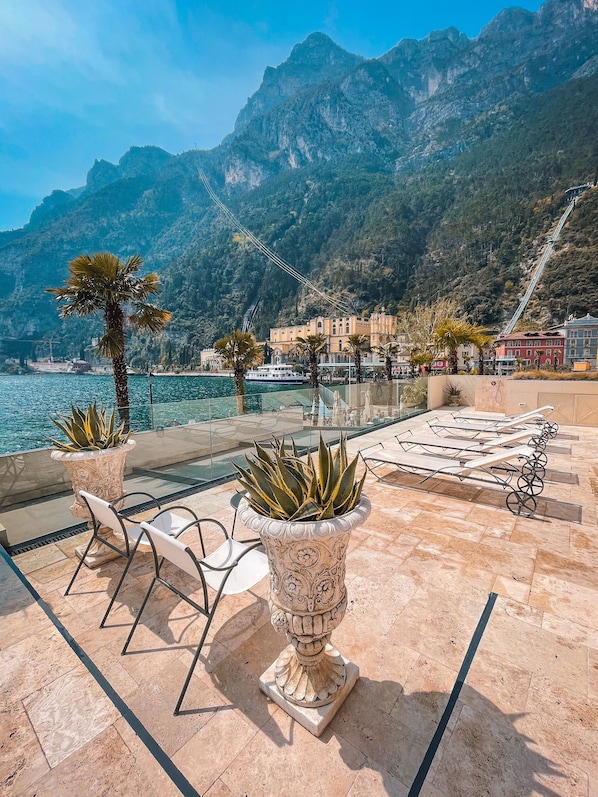 A terrace with a view of the sea and mountains, featuring a palm tree, a potted plant, and outdoor furniture.