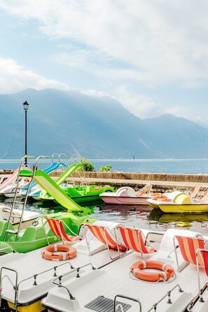 A row of colorful pedal boats docked at a pier with mountains in the background.