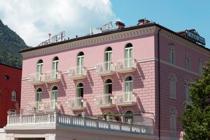 Un bâtiment rose doté de balcons, une enseigne indiquant « HÔTEL », et une montagne en arrière-plan.