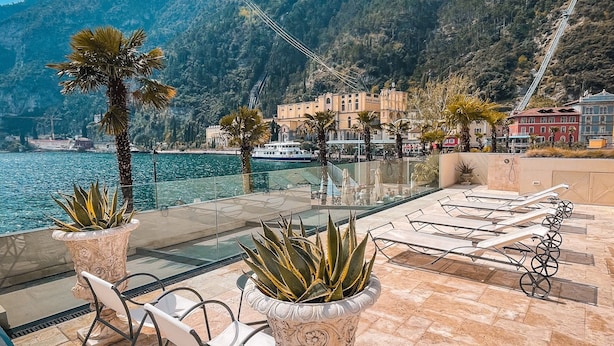 A terrace with a view of the sea and mountains, featuring potted plants and outdoor furniture.