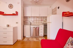 A compact kitchen with white cabinets, a dishwasher, and a red sofa.