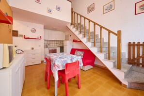 A dining area with a table and chairs, a staircase, and a kitchen in the background.