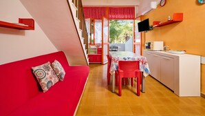 Eine Küche mit Esstisch, Stühlen und einer roten Couch mit gemusterten Kissen.