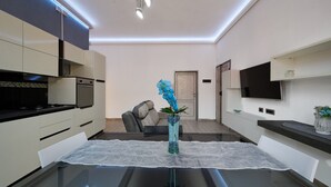 A modern kitchen with built-in appliances, a dining table with a glass top, and a vase with flowers. - Apartment 'Holy Days' with Balcony, Wi-Fi and Air Conditioning (Piombino)