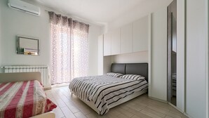 A bedroom with a bed, a bedside table, a mirror, a window with curtains, and a wardrobe. - Apartment 'Holy Days' with Balcony, Wi-Fi and Air Conditioning (Piombino)