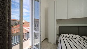 A bedroom with a bed, a window with a view of buildings, and a sliding door. - Apartment 'Holy Days' with Balcony, Wi-Fi and Air Conditioning (Piombino)
