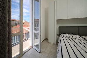 A bedroom with a bed, a window with a view of buildings, and a sliding door. - Apartment 'Holy Days' with Balcony, Wi-Fi and Air Conditioning (Piombino)