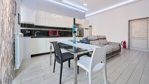 A modern kitchen with white cabinets, a dining table with chairs, and a sofa in a living area. - Apartment 'Holy Days' with Balcony, Wi-Fi and Air Conditioning (Piombino)