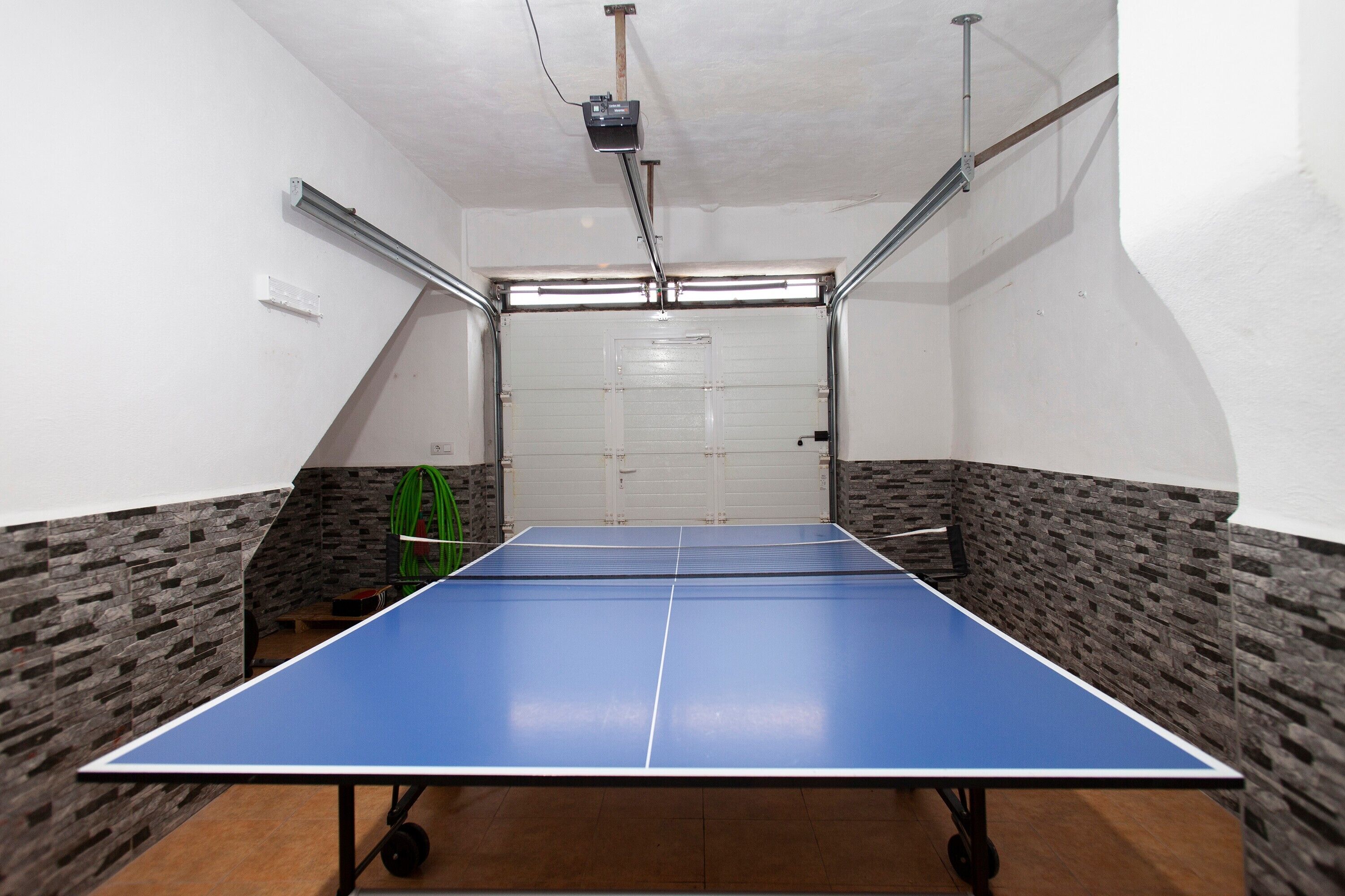 Una mesa de ping pong en una habitación con paredes de piedra y una puerta de garaje al fondo.