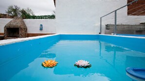 Una piscina con dos flores de loto, un horno de piedra y una pared blanca con detalles azules.
