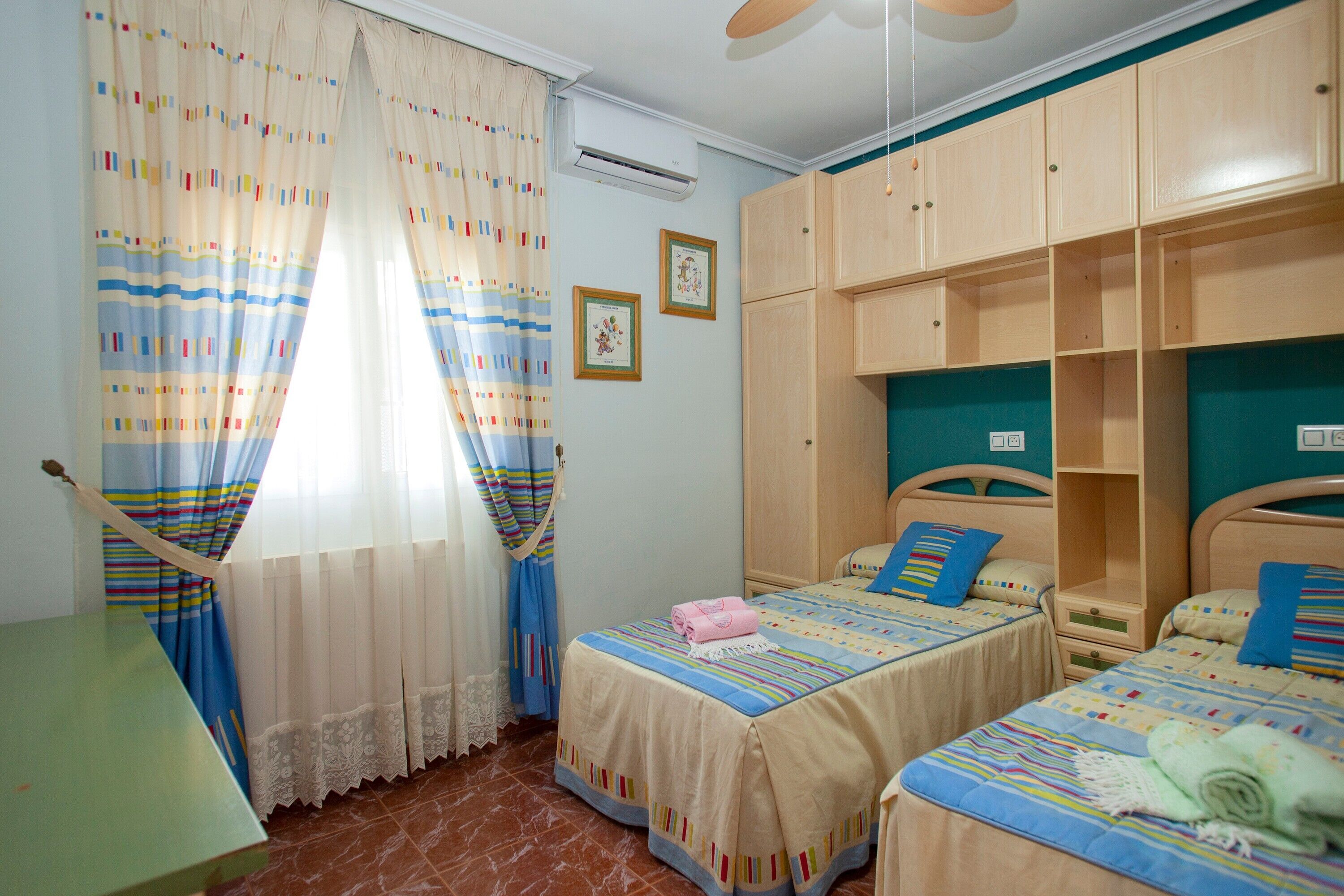 Une chambre avec deux lits, une armoire en bois, un bureau et une fenêtre avec des rideaux.