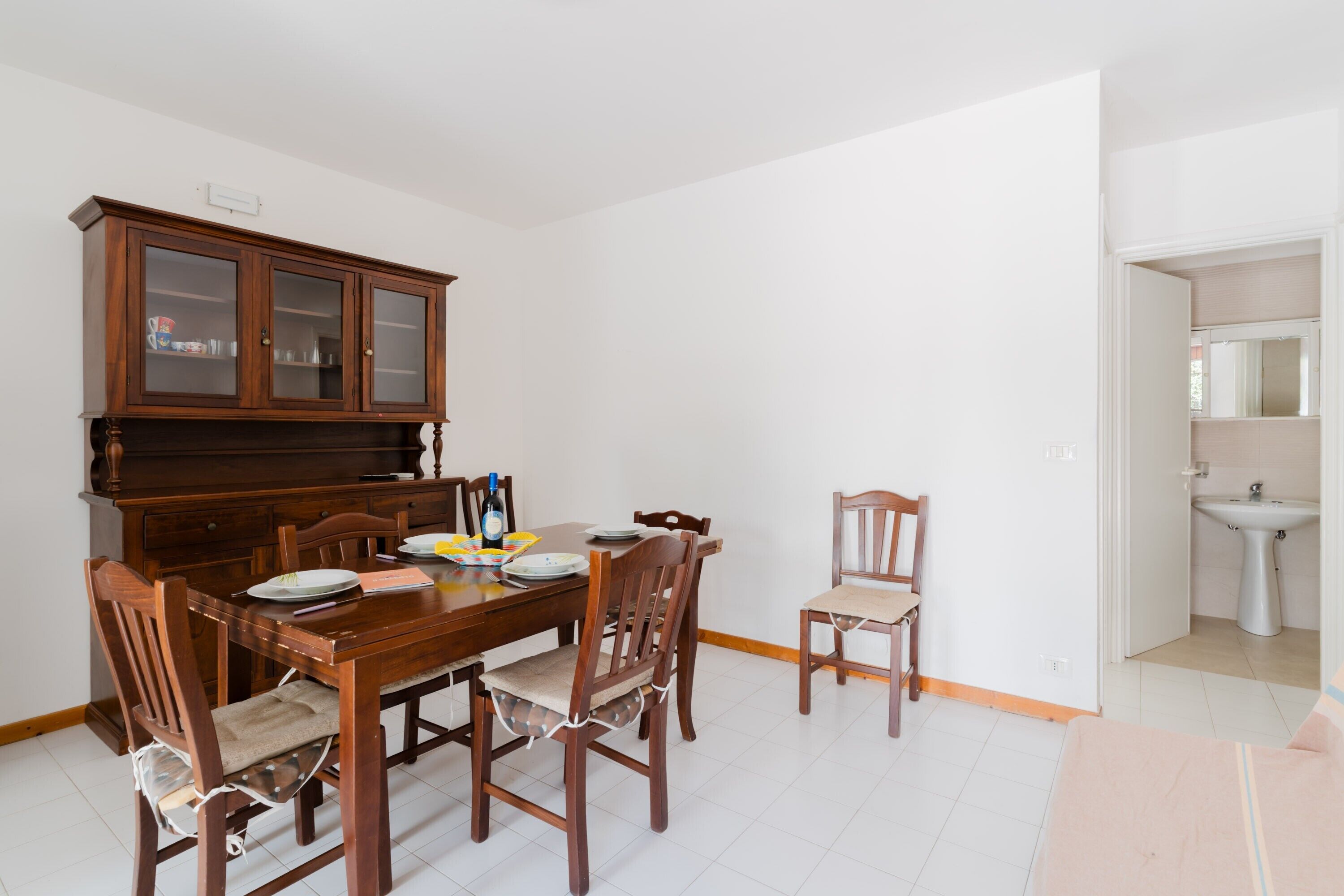 Un comedor con una mesa de madera, sillas, un armario y un lavamanos en la habitación contigua.