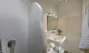 Un baño con ducha, lavamanos, espejo y toallero.