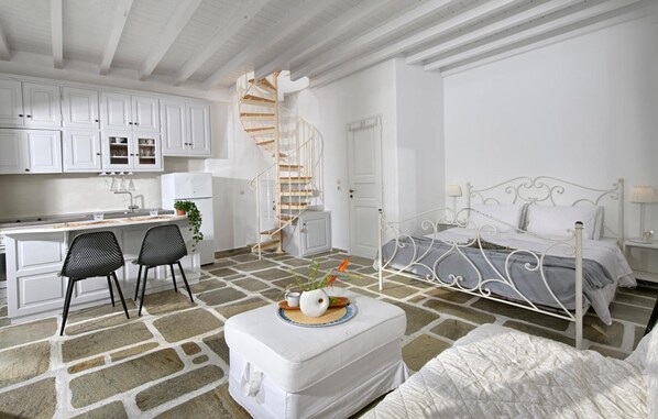 A room with a bed, a desk, two chairs, a white cabinet, a spiral staircase, and a stone-patterned floor.