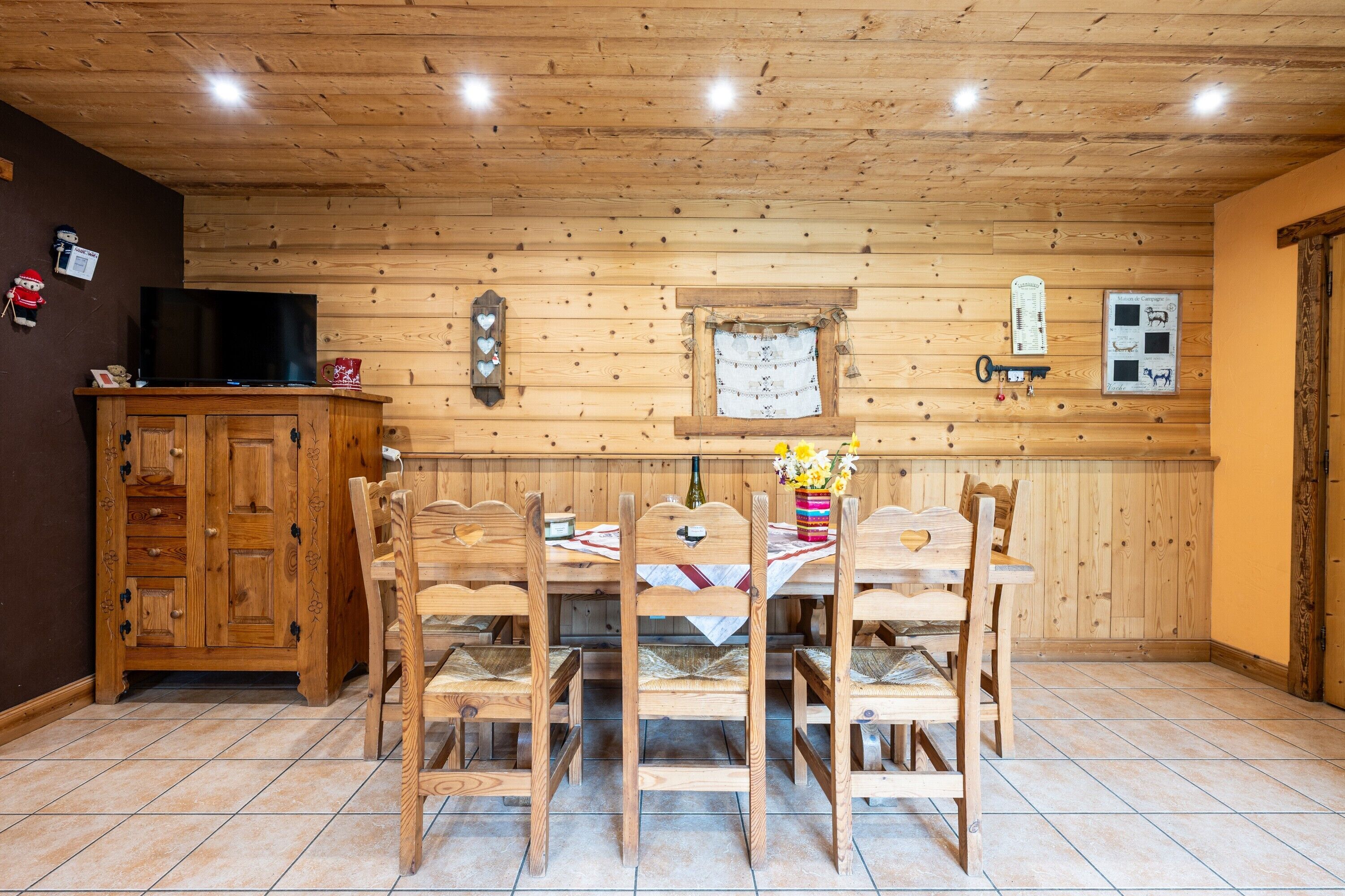 Ein Zimmer mit Holzwänden, einem Esstisch, Stühlen, einem Fernseher und einem Schrank.
