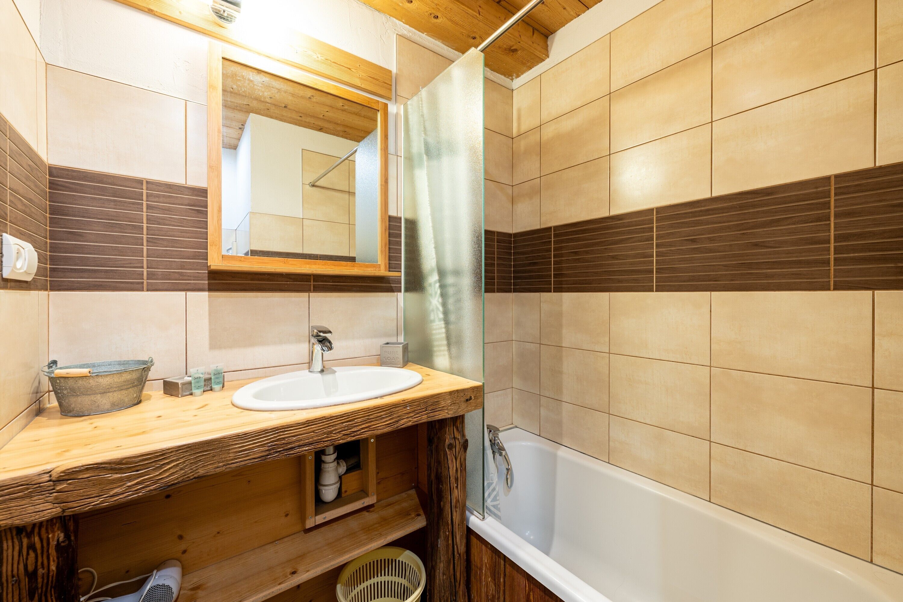 Ein Badezimmer mit einem Holzkosmetikschrank, einem weißen Waschbecken, einem Spiegel und einer Badewanne.