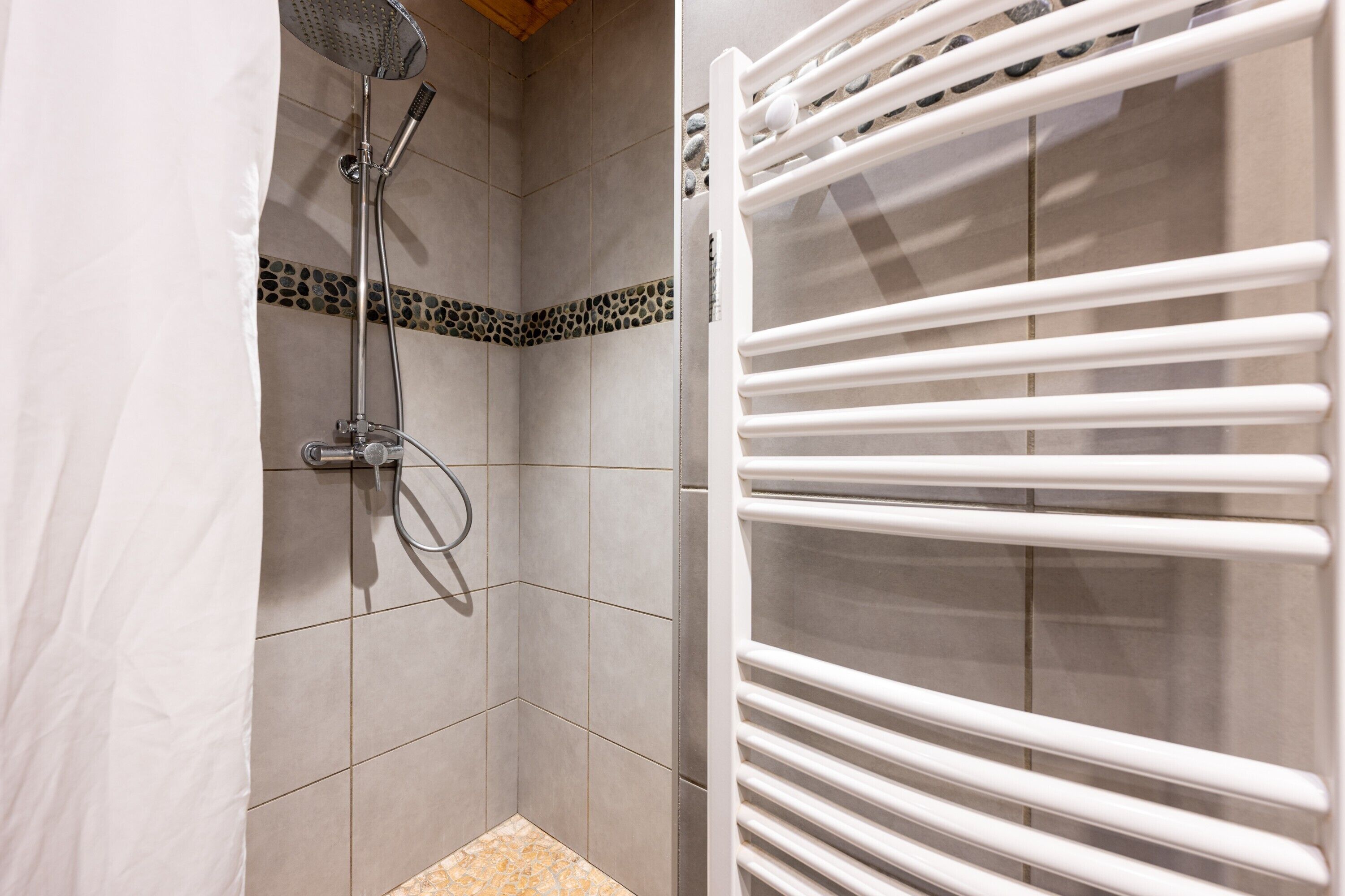 A shower with a handheld showerhead, a tiled floor, and a white towel rack.