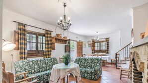 Un salón amplio con sofás de estampado verde, una mesa de vidrio, sillas de madera y una escalera.