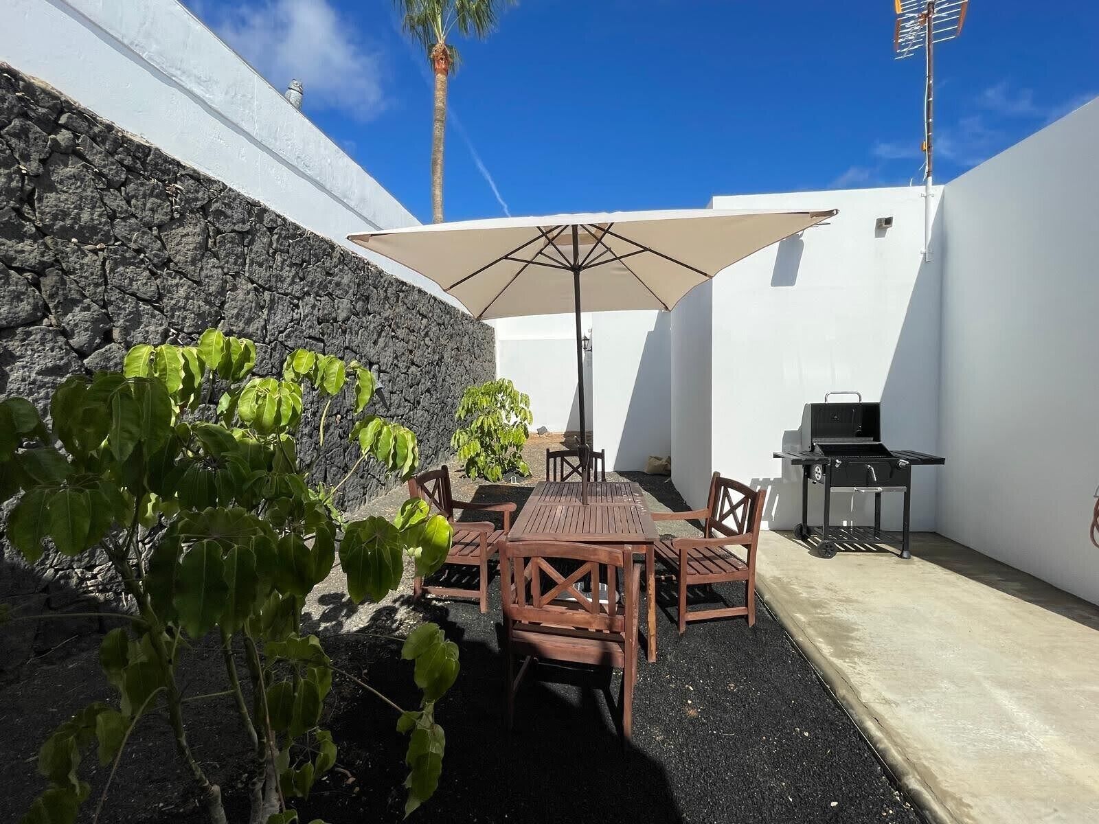 A patio with a table and chairs, a grill, and a stone wall.