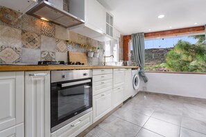 Una cocina moderna con horno empotrado, armarios blancos y ventana con vistas a un jardín.