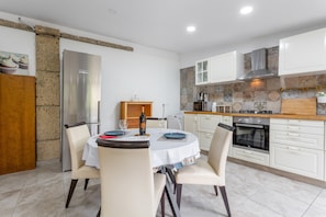 Una cocina moderna con gabinetes blancos, un refrigerador de acero inoxidable, una encimera de madera y una zona de comedor con una mesa redonda y sillas.
