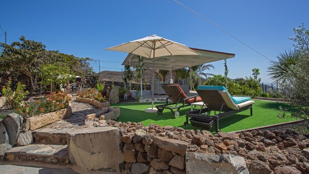 Un espace patio avec une piscine, des chaises longues et une pergola dotée d’un parasol.