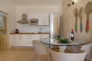 A modern kitchen with white cabinets, a stainless steel refrigerator, a microwave, and a glass dining table with chairs.