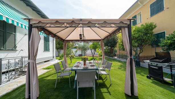 Un patio techado con una mesa dispuesta para cuatro personas, sillas alrededor y una parrilla al fondo.