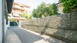 Un estrecho callejón con una pared de piedra texturizada, un camino de hormigón y edificios residenciales al fondo.
