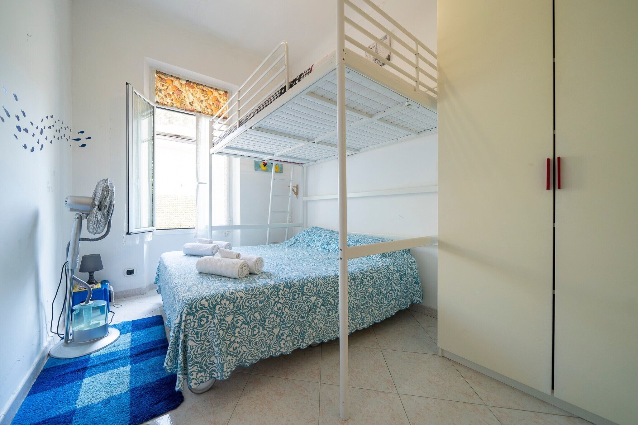 A bunk bed room with a window, a fan, and a blue checkered rug.
