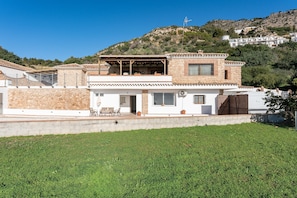 Ein modernes Haus mit einer Stein-Fassade, einer überdachten Terrasse und Blick auf einen Hügel.