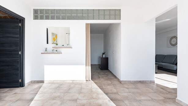 A modern interior with a tiled floor, a black door, a hallway leading to a living area, and a wall-mounted shelf with decorative items. - Apartment 'Timón' with Sea View, Wi-Fi and Air Conditioning (Mijas)