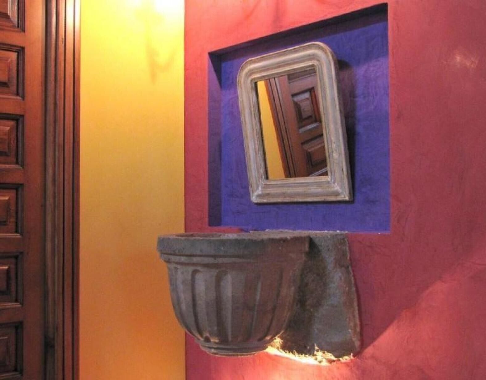 Un baño con puerta de madera, un espejo y un lavamanos empotrado.