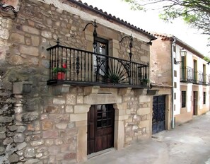 A stone building with a wooden door, a balcony with a wrought iron railing, and a small potted plant.