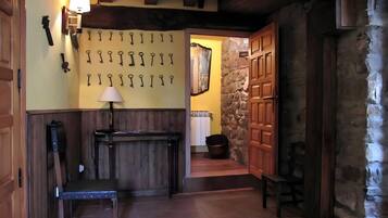 A hallway with a wall-mounted key rack, a wooden bench, a table with a lamp, and a stone wall.