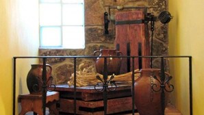 Un interior rústico con una pared de piedra, un barril de madera y una baranda de metal.