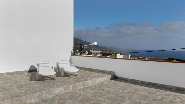 Eine Dachterrasse mit zwei weißen Lounge-Stühlen, Blick auf das Meer und einem Berg in der Ferne.