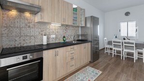Eine moderne Küche mit Holzschränken, einem Edelstahlkühlschrank und einem Essbereich mit weißen Stühlen.