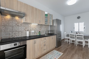 Una cocina moderna con armarios de madera, un refrigerador de acero inoxidable y un comedor con sillas blancas.
