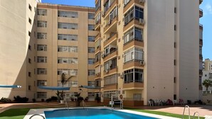 A swimming pool with a metal ladder, surrounded by a grassy area and a multi-story building with balconies. - Studio Apartment 'Centro Torremolinos' with Shared Pool, Wi-Fi and Air Conditioning (Torremolinos)