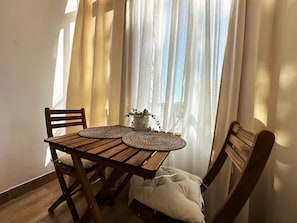 Een houten tafel met twee gevlochten onderzetters, een plant in pot en een bank met kussen.