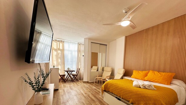 A hotel room with a bed, a TV, a ceiling fan, a dining area with chairs, and a window with curtains. - Studio Apartment 'Centro Torremolinos' with Shared Pool, Wi-Fi and Air Conditioning (Torremolinos)