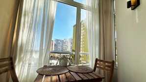 A wooden table with woven placemats, two wooden chairs, a potted plant, and sheer curtains. - Studio Apartment 'Centro Torremolinos' with Shared Pool, Wi-Fi and Air Conditioning (Torremolinos)